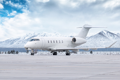 White luxury executive aircraft taxiing on airport taxiway in winter on the background of high picturesque snow capped mountains