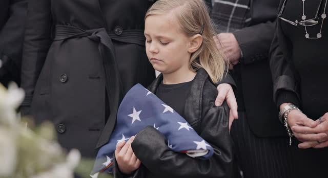 Funeral, cemetery and child with American flag for veteran for respect, ceremony and memorial service. Family, depression and sad girl by coffin in graveyard mourning military, army and soldier hero
