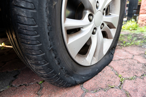 Closeup of deflated flat car tire with rupture at the side of the wheel