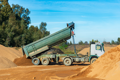Tilting truck for transporting aggregates with the raised box unloading sand in a quarry.