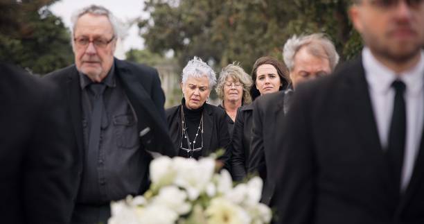 istock Pallbearers, men and walking with coffin in funeral, ceremony or mourning event at graveyard with sad, grief and flowers. People, support and walk with family in memorial service together with casket 2045430778