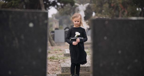 sad, death or kid in cemetery for funeral. spiritual service or grave visit for respect in christian religion. mourning, tomb or depressed girl child outside in graveyard for grief, loss or farewell - child grief mourner disappointment - fotografias e filmes do acervo