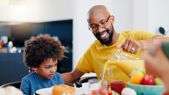 Black family, juice and parents with child for breakfast, lunch and eating together in home. Happy, food and drink and dad and boy at table for bonding for health, nutrition and hunger in house