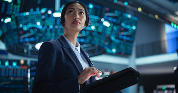 istock Portrait of a Young Beautiful Stock Exchange Broker Using Tablet Computer, Researching Real-Time Stocks Data, Analyzing Commodities and Exchange Market Charts. Professional Investment Banker in Office 2045439411