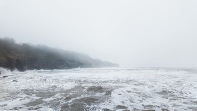 Very mist and foggy scene on the coast of the UK. Winters coastal seascape with small boats and rough seas crashing against the rocks and cliffs on the east coast of the UK. English cold spell