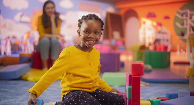 Cheerful African Girl Playing with Colorful Building Blocks in Kindergarten. Beautiful Black Child Posing, Looking at Camera and Smiling. Happy Children Playing in Modern Daycare Center