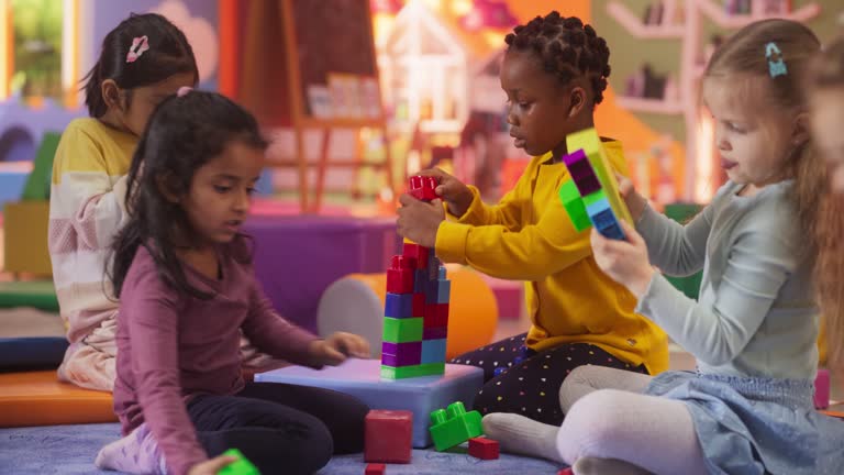 Portrait of a Group of Diverse Kids Playing with Colorful Building Blocks in Daycare Center. Cute Little Creative Girls Focused on Making a Magical Toy House. Childhood and Kindergarten Concept