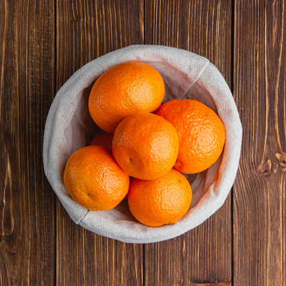 Tangerines in a straw basket on a brown rustic wooden table. Top view of fresh mandarins.