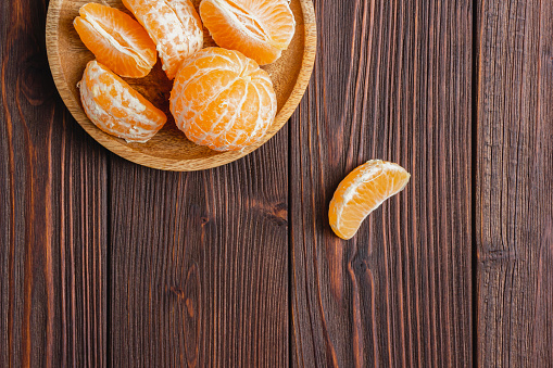 Tangerines on a plate on a brown rustic wooden table. Top view of fresh mandarins.