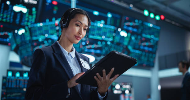 istock Young Asian Female Broker Working on Tablet Computer on Stock Exchange Floor. Traders Monitoring Real-Time Stocks, Commodities and Exchange Market Data. Professional Investment Agents in Office 2045456603