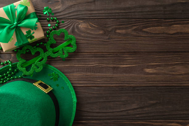 Magical St. Patrick's display, with top view clovers, leprechaun hat, gift parcel, celebratory eyewear, strands of beads, and confetti, neatly presented on a timber backdrop for text