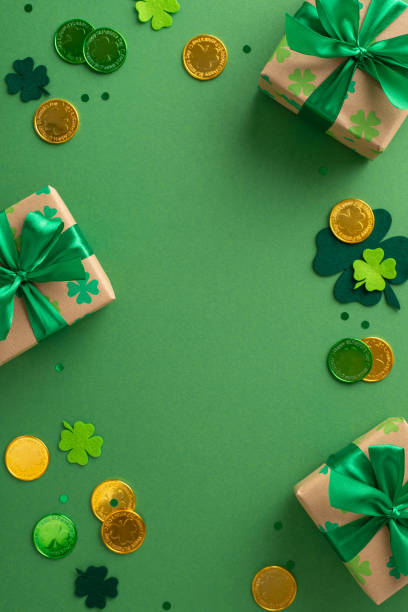 istock St. Patrick's day vertical magical display from top view, with shamrocks, gold coins, festooned boxes, and confetti, arranged on a green tableau, with space for copy 2045456645