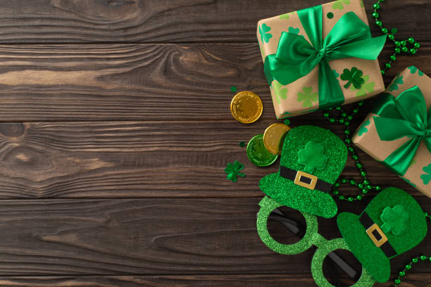 istock Captivating St. Patrick's arrangement from top-view, with shamrocks, wealth coins, parcels, masquerade glasses, necklaces, and confetti, arrayed on wood plank background, with void for text or ads 2045456647