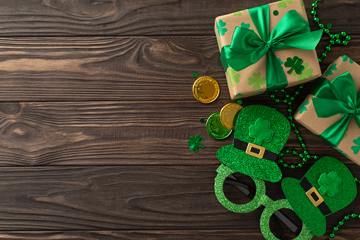 Captivating St. Patrick's arrangement from top-view, with shamrocks, wealth coins, parcels, masquerade glasses, necklaces, and confetti, arrayed on wood plank background, with void for text or ads