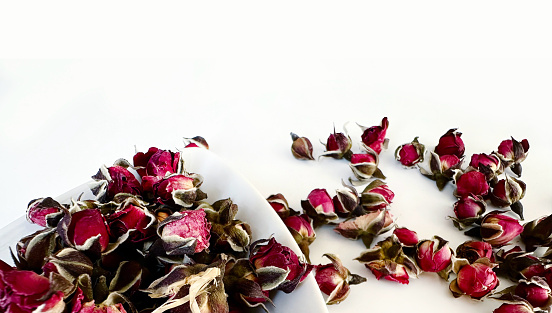 Dry rose bud tea flowers in the triangle plate on white background, corner frame decoration. Scattered flowers