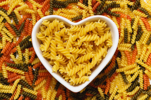 Raw pasta fusilli in heart bowl on torti texture. Top view of Italian cuisine ingredient.