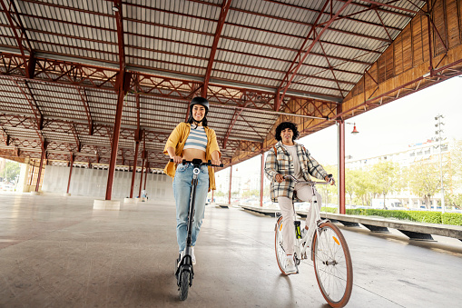 Cheerful multicultural travelers are riding rent a bike and an electric scooter during their visit to Spain.