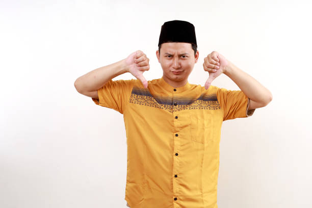 istock Unhappy Young asian man wearing typical muslim clothes standing while showing thumbs down isolated on white background 2045488486