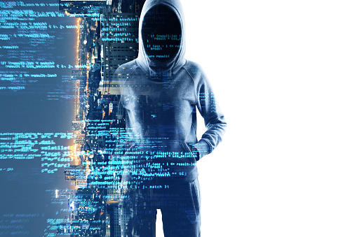 Mysterious cyber hacker with obscured face standing before a screen with futuristic blue digital code signifying cybercrime and security breach
