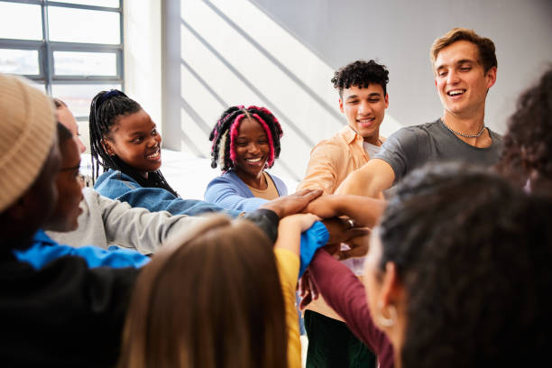 Diverse group of smiling young college students standing together in a huddle with their hands in a stack at school