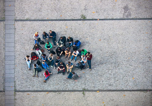 Paris, France - 10 26 2013: A group of 26 young people in casual clothes with backpacks sitting together on the pavement of the Place Georges Pompidou in Paris. Top view