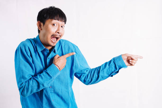 Young man wearing casual green tshirt and looking at the camera pointing with hands and fingers to the side.