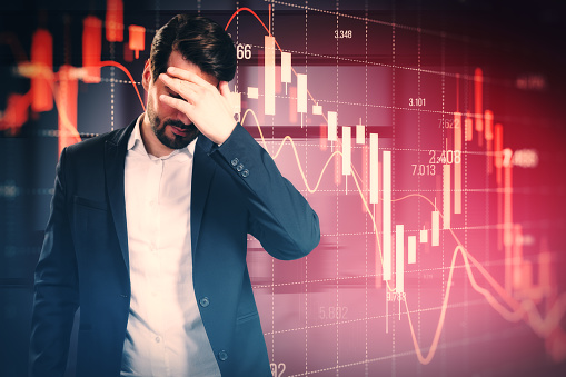 Stressed out man with falling red forex candlestick chart on blurry background. Global economic recession, stock market crash, inflation concept