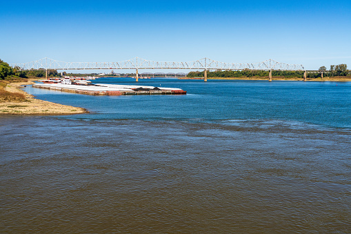 Barges wait at the confluence of the blue Ohio river and brown Mississippi river at Cairo with blue and brown muddy streams mixing