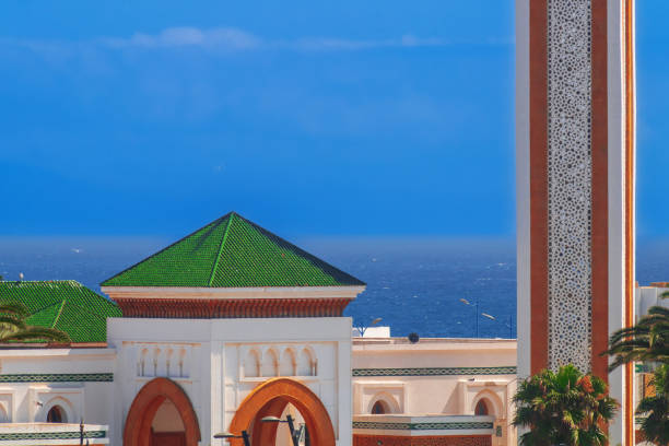 Architectural features of Moroccan mosques in the form of different decor elements and colors used in decoration. In the middle and background, ocean and a blue hazy sky with some cloudiness.