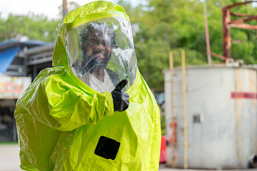 Expert in a hazmat suit stands confidently within a factory, giving a reassuring thumbs up before undertaking a critical job. Chemical, Safety, and Protective Workwear underlining the high-stakes nature of the expert's responsibilities.