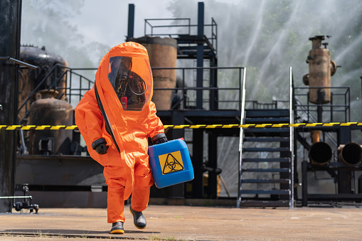 Dedicated chemical exterminator, clad in a hazmat suit, carefully carrying a gallon of chemicals out of a factory. Essence of danger and precision involved in chemical extermination processes, with keywords like Chemical, Toxic Waste, and Danger underscoring the gravity of the task at hand.