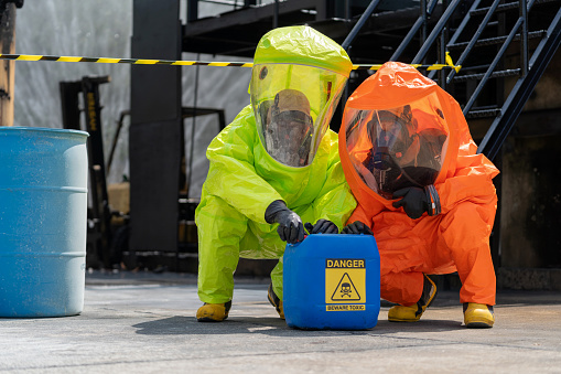 Experts donned in chemical protective suits, is diligently working to recover gallons of chemicals from the area surrounding a chemical plant. The urgent mission is to prevent potential explosions, showcasing the keywords Chemical, Danger, and Emergency Services Occupation to emphasize the gravity of the situation.