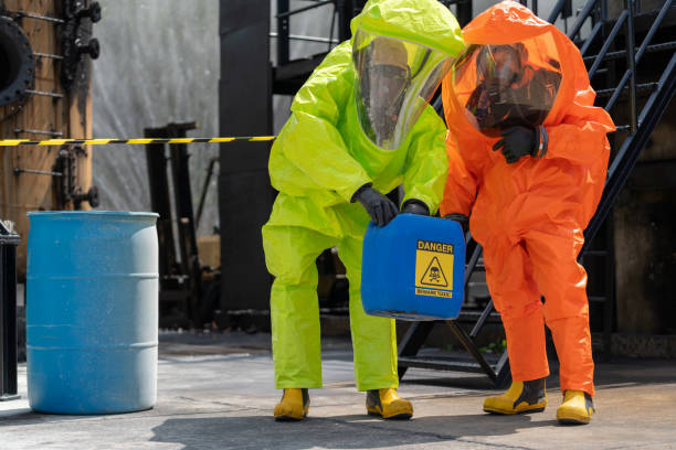 safely extracting chemical drum from oil plant. a skilled group of expert worker in hazmat suit including advanced protective gear, in action as they work collaboratively to remove a chemical drum from the oil plant, enveloped in a curtain of water. - radiation protection suit toxic waste protective suit cleaning photos et images de collection