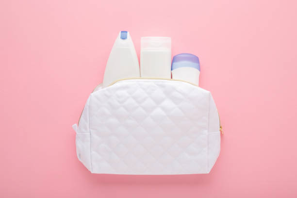 istock White cosmetic travel bag with plastic bottles on light pink table background. Pastel color. Care about clean and body skin. Female beauty products. Closeup. Top down view. 2045587713