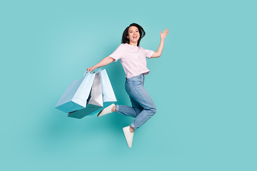 Full length photo of funky pretty metis mixed race woman wear pink t-shirt rising bargains jumping high isolated turquoise color background.