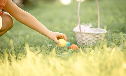 Little cute girl holding basket with colorful painted eggs on Easter egg hunt in park.