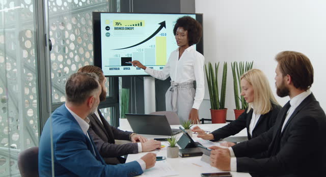 Beautiful african american woman reporting about business concept of joint project in front of her concentrated high-skilled colleagues in meeting room