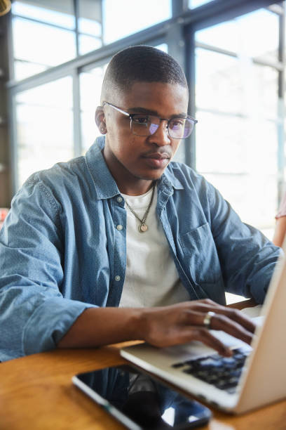 Young male college student using a laptop at a table in a school cafeteria