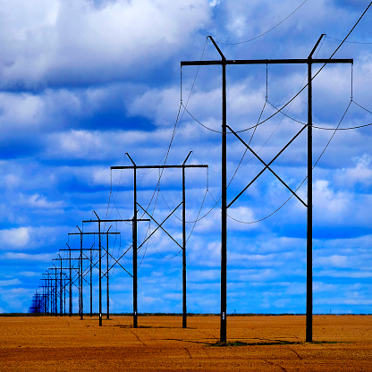 Powerlines in field with blue sky and clouds representing utility