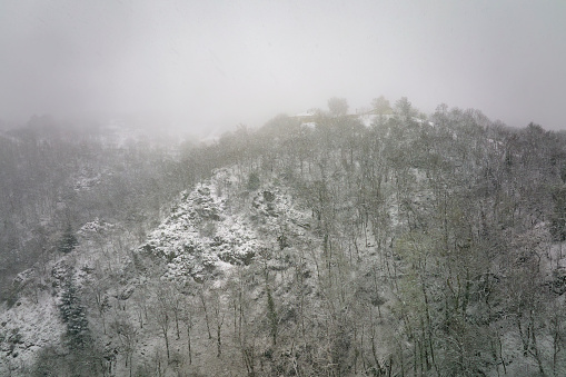 Aerial foggy landscape with mountain cliffs covered with fresh fallen snow during heavy snowfall in winter mountain forest on cold quiet day.