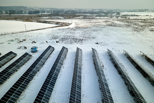 Aerial view of electrical power plant with solar panels covered with snow melting down in winter end for producing clean energy. Concept of low effectivity of renewable electricity in northern region.