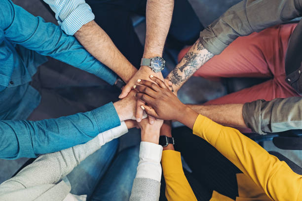Growing the company together Group of business persons standing in a circle and stacking hands hands clasped stock pictures, royalty-free photos & images