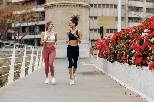 Two smiling women athlete running side by side along an outdoor track on buildings background