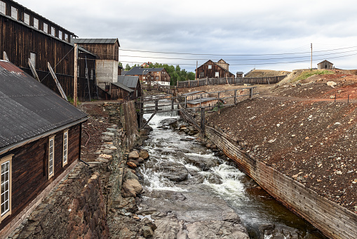 Roros mining landscape, where the forceful Glomma River cuts through, framed by weathered wooden buildings and mining remnants. Norway