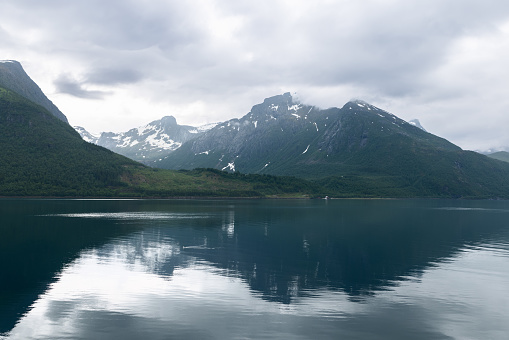 The stillness of a Norwegian fjord reflects the cloudy sky and shadowy mountains, creating a contemplative and moody landscape tableau