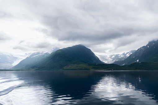 The stillness of a Norwegian fjord reflects the imposing silhouette of the Svartisen Glacier, a serene and moody tableau amidst the vast wilderness