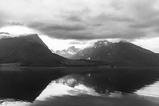 Monochromatic hues enhance the solemn beauty of a Norwegian fjord, where reflective waters and mountain silhouettes merge under a dramatic sky
