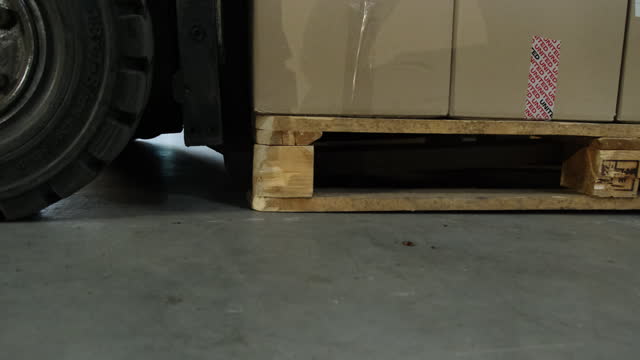 Forklift lowers cardboard boxes with products in warehouse