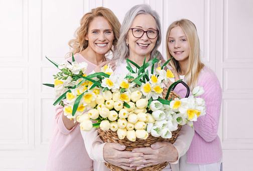 On celebration of Mother's Day, granddaughter and her mother present bouquet of spring flowers to grandmother. Their hugging and joying symbolize connection of three generations of mothers