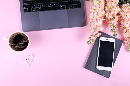 Cropped shot of feminine workspace with laptop, matthiola flowers and cup of black coffee. A bouquet for international women's day in the office. Pink background, copy space, flat lay, close up.